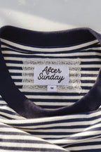 Close-up of a navy and white striped t-shirt with a white lace-trimmed neck label that reads 'After Sunday' and size 'M'.

