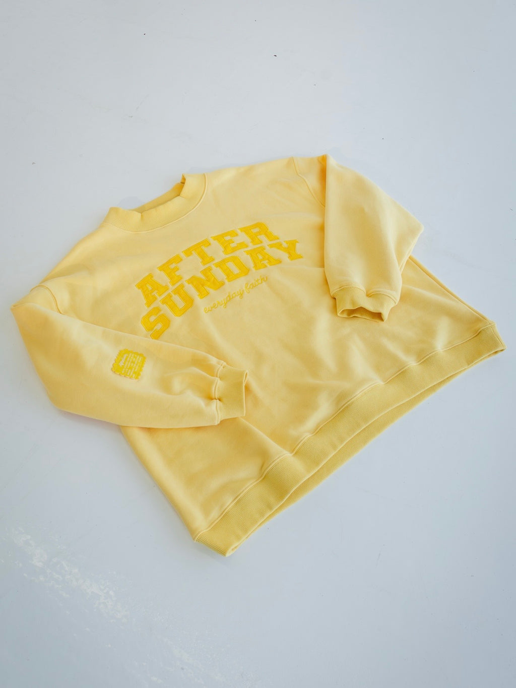 A butter yellow crewneck sweatshirt with 'AFTER SUNDAY' printed in yellow on the front, laid flat on a light gray background.

