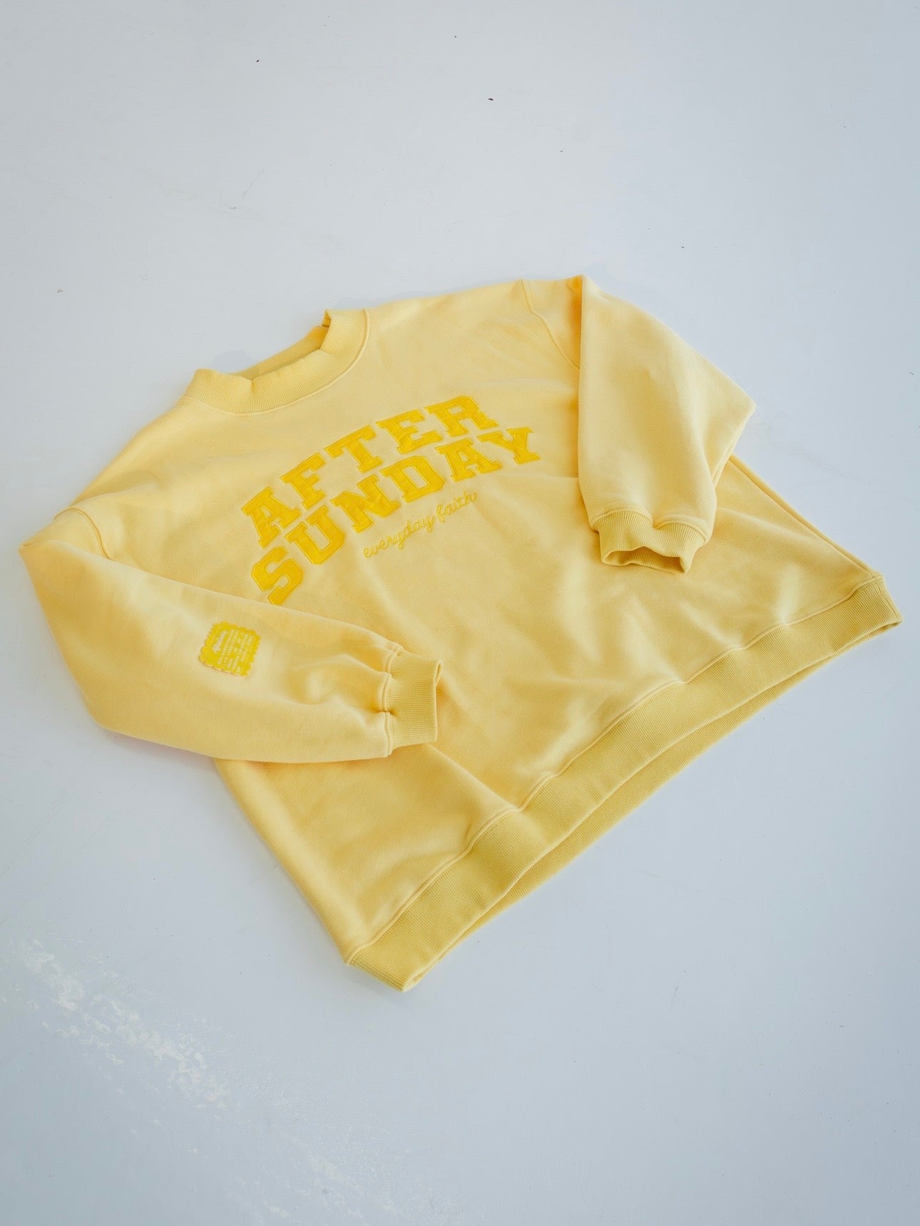 A butter yellow crewneck sweatshirt with 'AFTER SUNDAY' printed in yellow on the front, laid flat on a light gray background.

